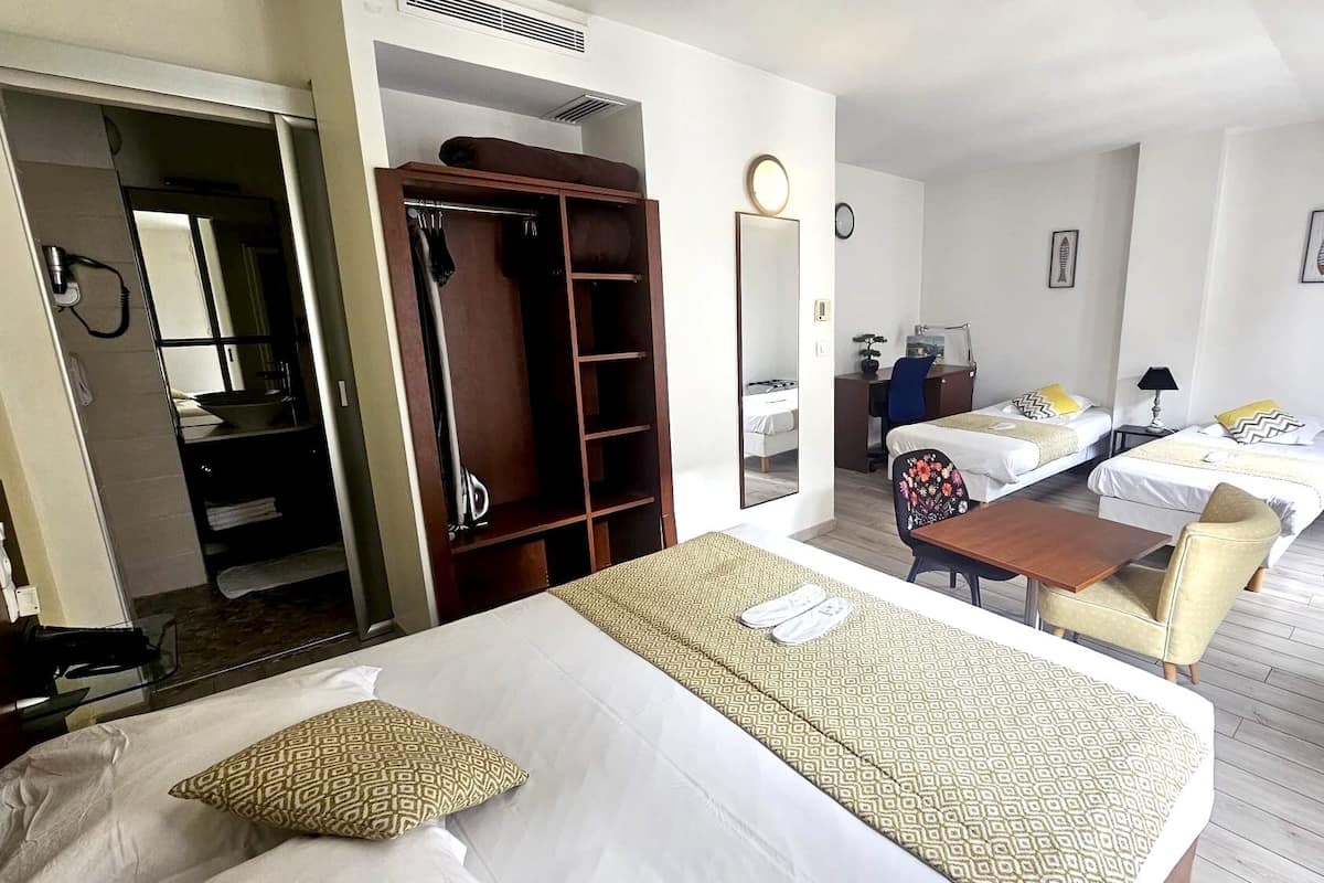 A hotel room with a large bed, a desk, two single beds, a wardrobe, a mirror, and a TV.