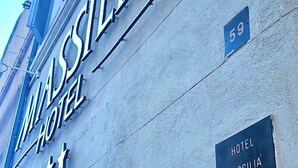 Het uiterlijk van Hotel Massilia, met een opvallend bord, een zichtbaar huisnummer en een raam met een lijst waarop de naam van het hotel staat.