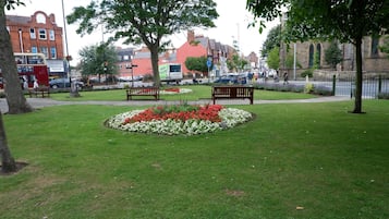 A park with benches, flower beds, and a red brick building in the background.