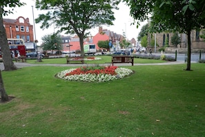 A park with benches, flower beds, and a red brick building in the background. - The Chimes (Bridlington)