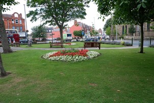 A park with benches, flower beds, and a red brick building in the background.