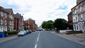 A residential street with terraced houses, parked cars, and a clear sky. - The Chimes (Bridlington)
