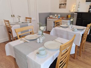 A dining area with tables set for two, each with white tablecloths, wooden chairs, and a vase with flowers. - The Chimes (Bridlington)