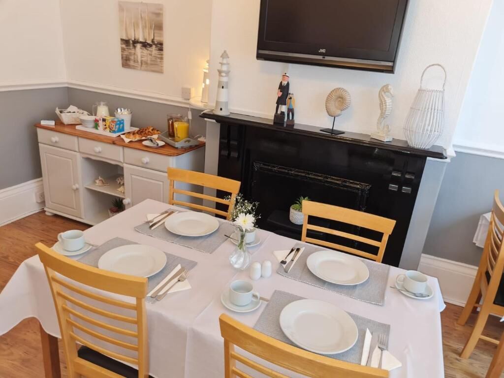 Un coin repas avec une table dressée pour quatre personnes, des chaises, une cheminée et un téléviseur fixé au mur.