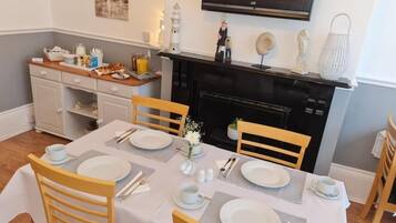 Un coin repas avec une table dressée pour quatre personnes, des chaises, une cheminée et un téléviseur fixé au mur.
