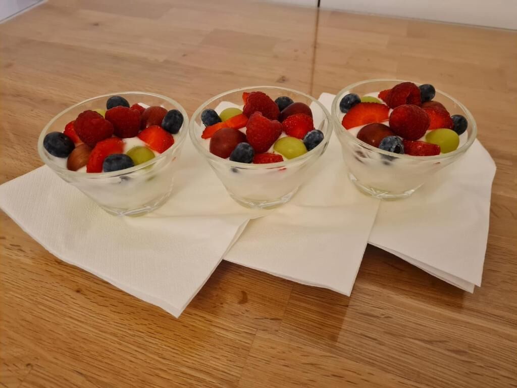 Three bowls of fruit salad on a wooden table with white napkins.