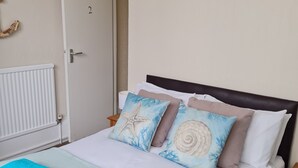 A hotel room with a bed, a painting of a beach house, and a door. - The Chimes (Bridlington)