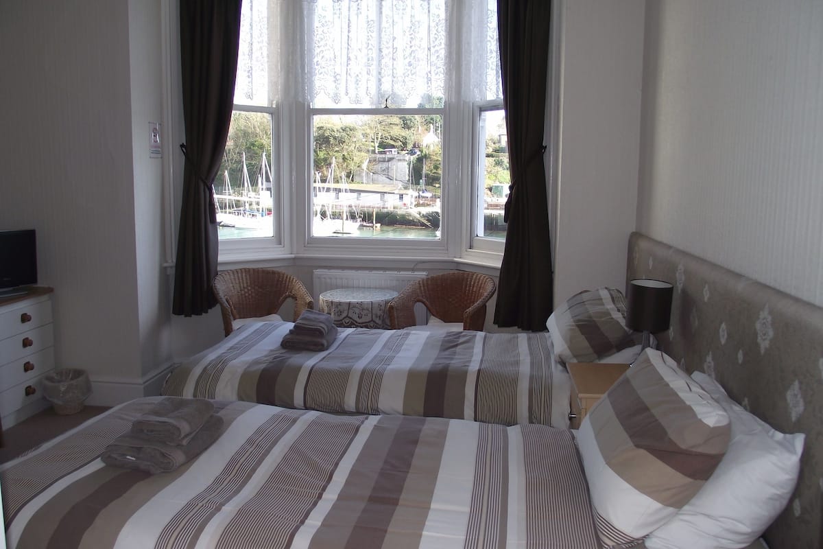 A bedroom with two beds, a window with curtains, a small table, and a chair.