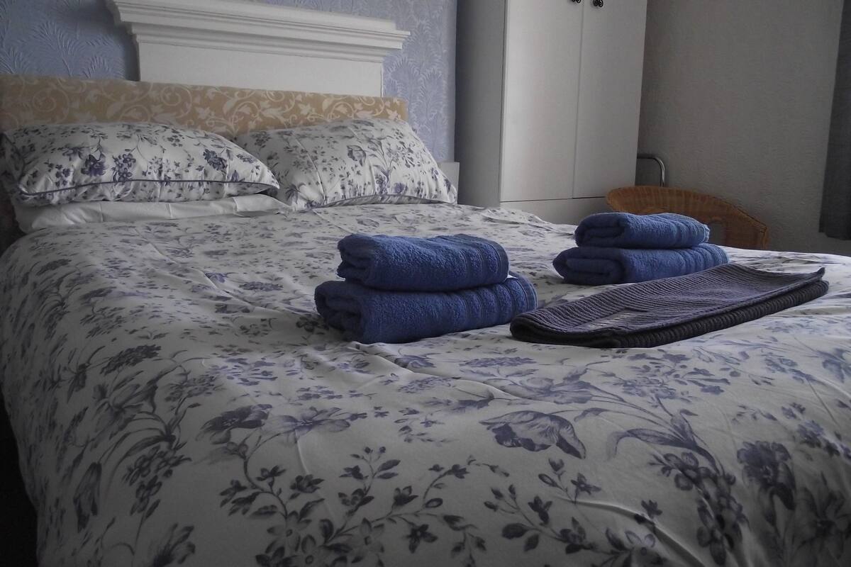 A neatly made bed with floral bedding, two rolled towels, and a black tray.