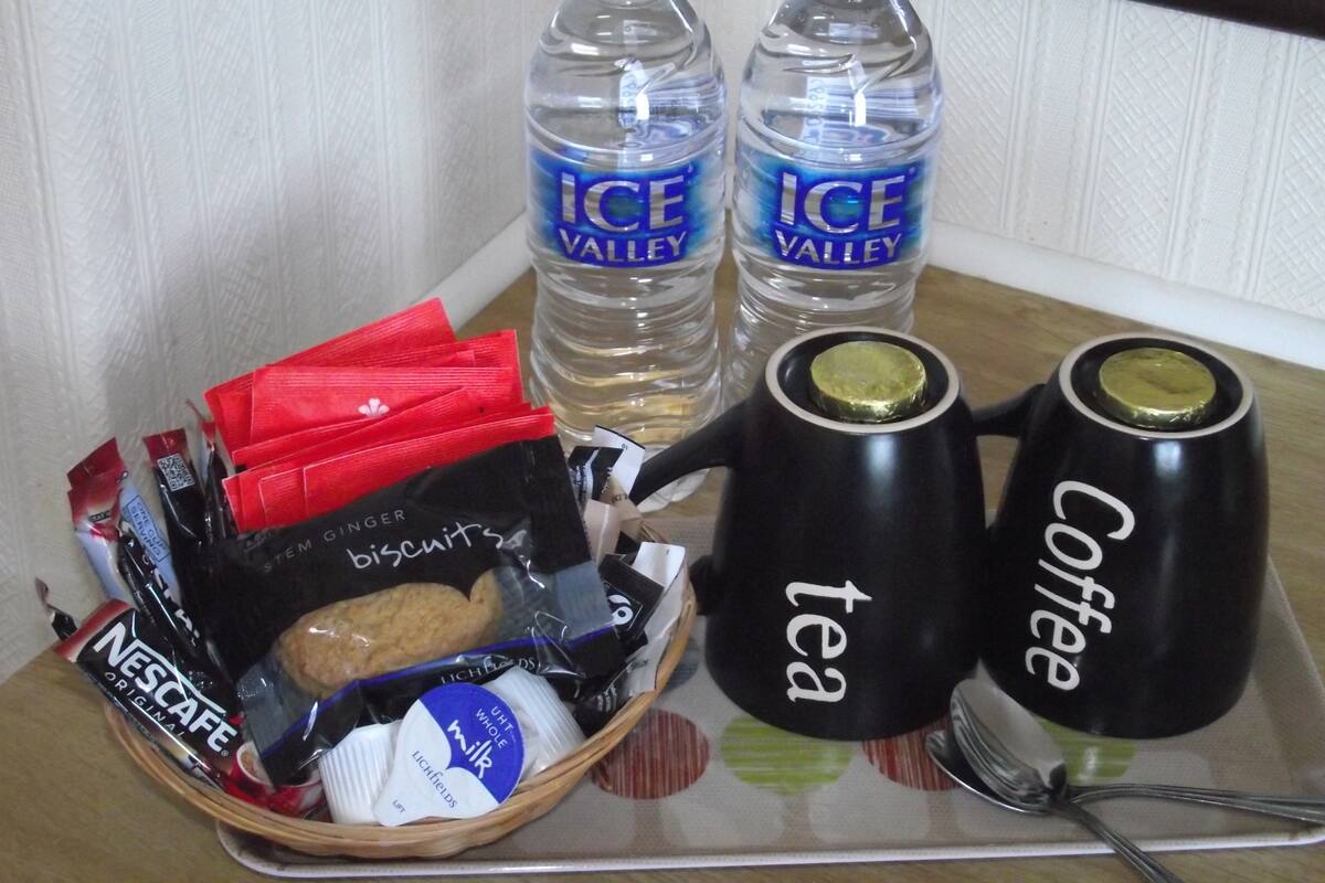 A tray with two bottles of ICE Valley water, a basket of snacks, and two black mugs labeled "tea" and "coffee".