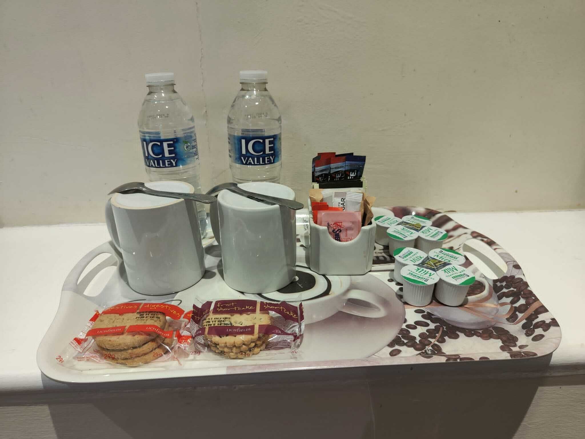 A tray with water bottles, mugs, a coffee maker, and packaged snacks.