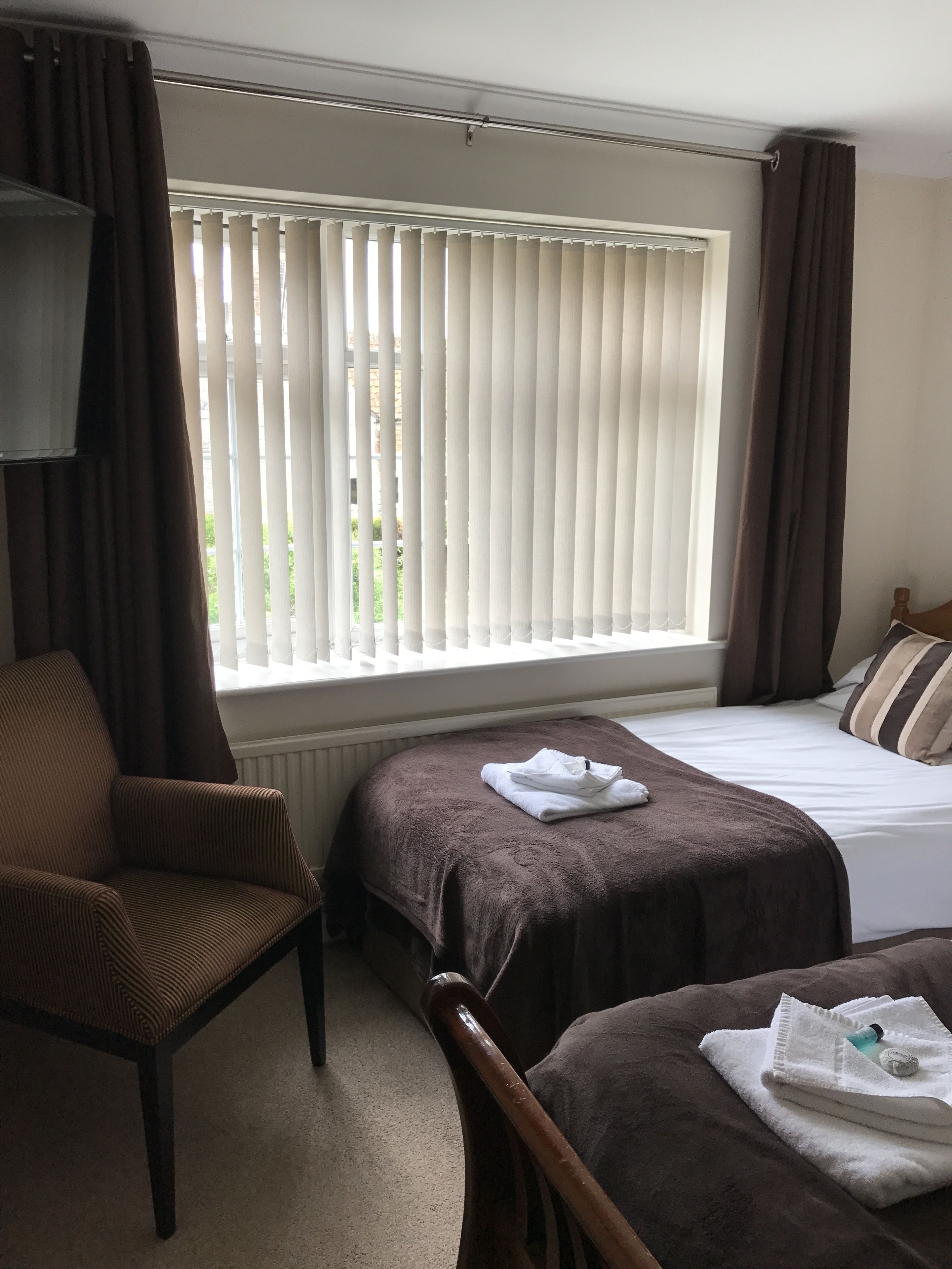 A hotel room with a bed, a chair, and a window with blinds.