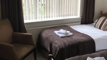 A hotel room with a bed, a chair, and a window with blinds.