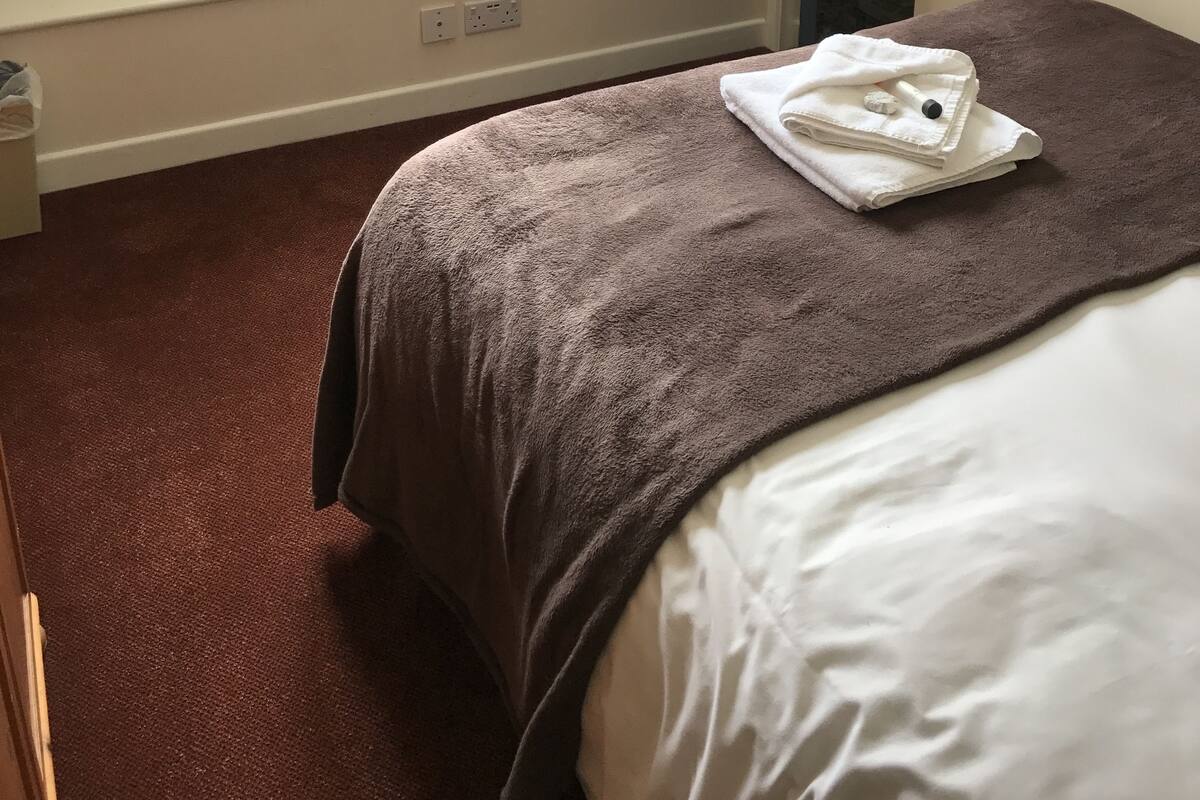 A hotel room with a bed, a window with curtains, a radiator, and a door.