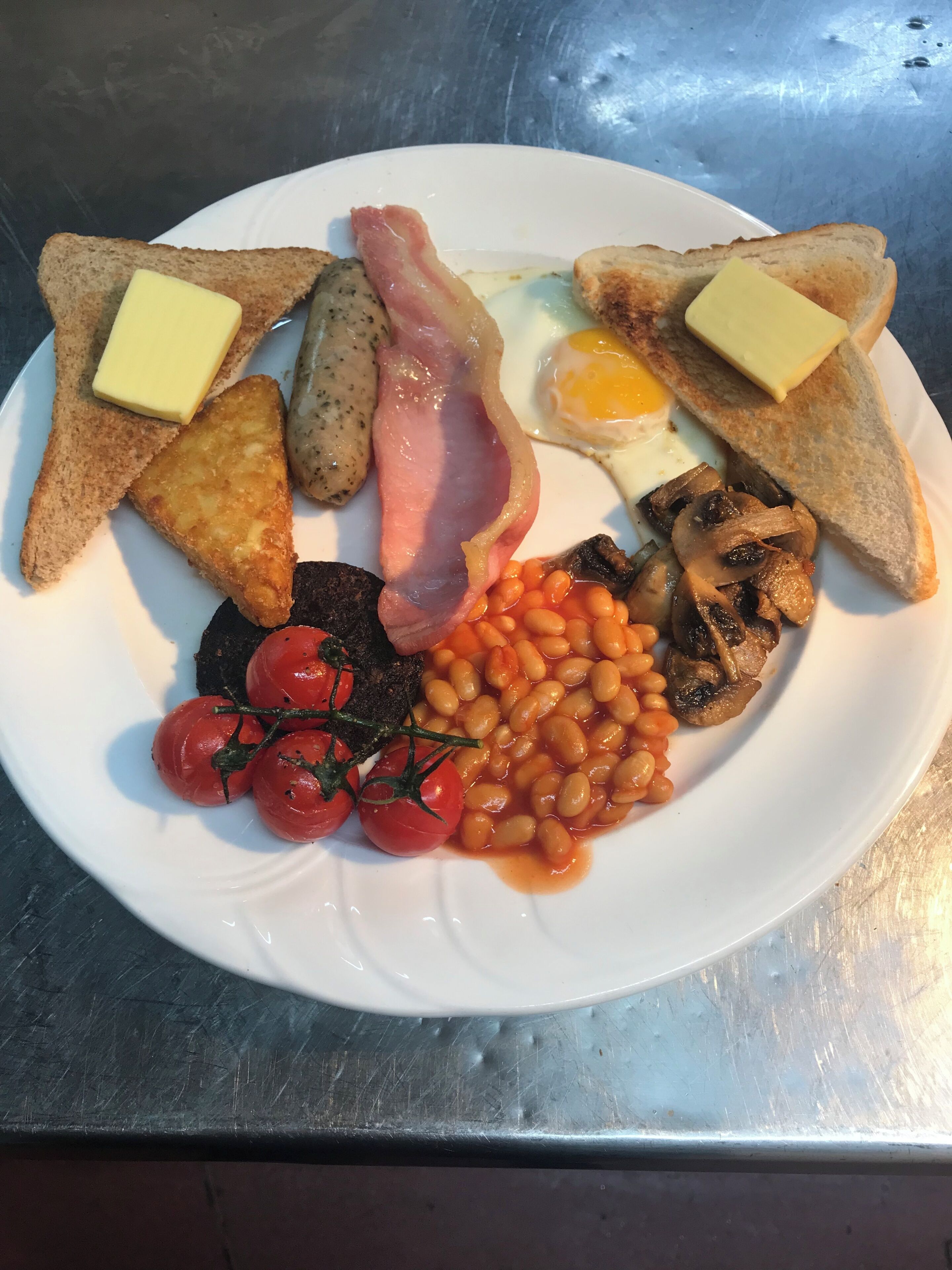A plate of breakfast food including toast, eggs, bacon, mushrooms, beans, and tomatoes.
