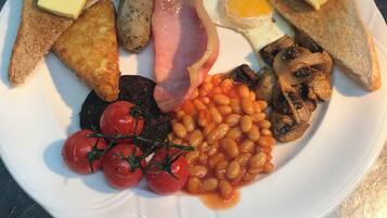 A plate of breakfast food including toast, eggs, bacon, mushrooms, beans, and tomatoes.
