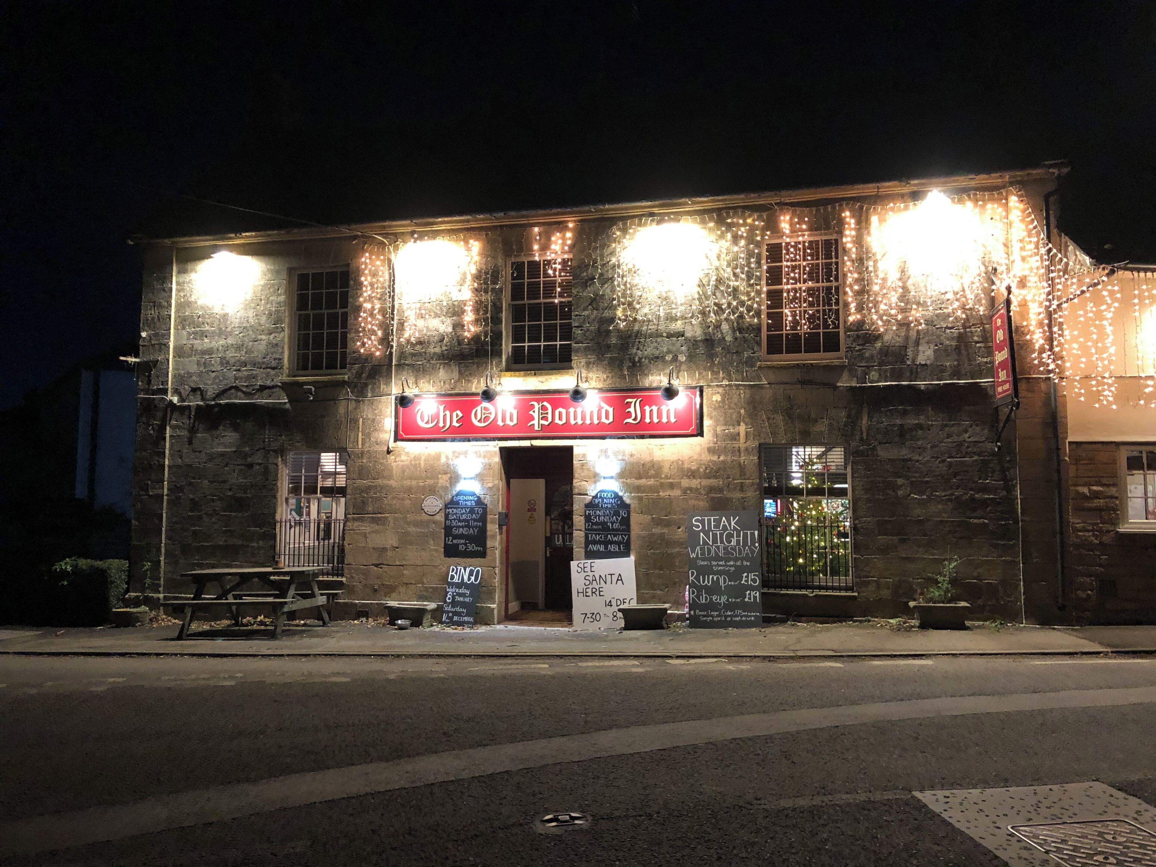 A building with a sign reading 'The Old Pound Inn,' featuring a brick facade, multiple windows, and outdoor seating.