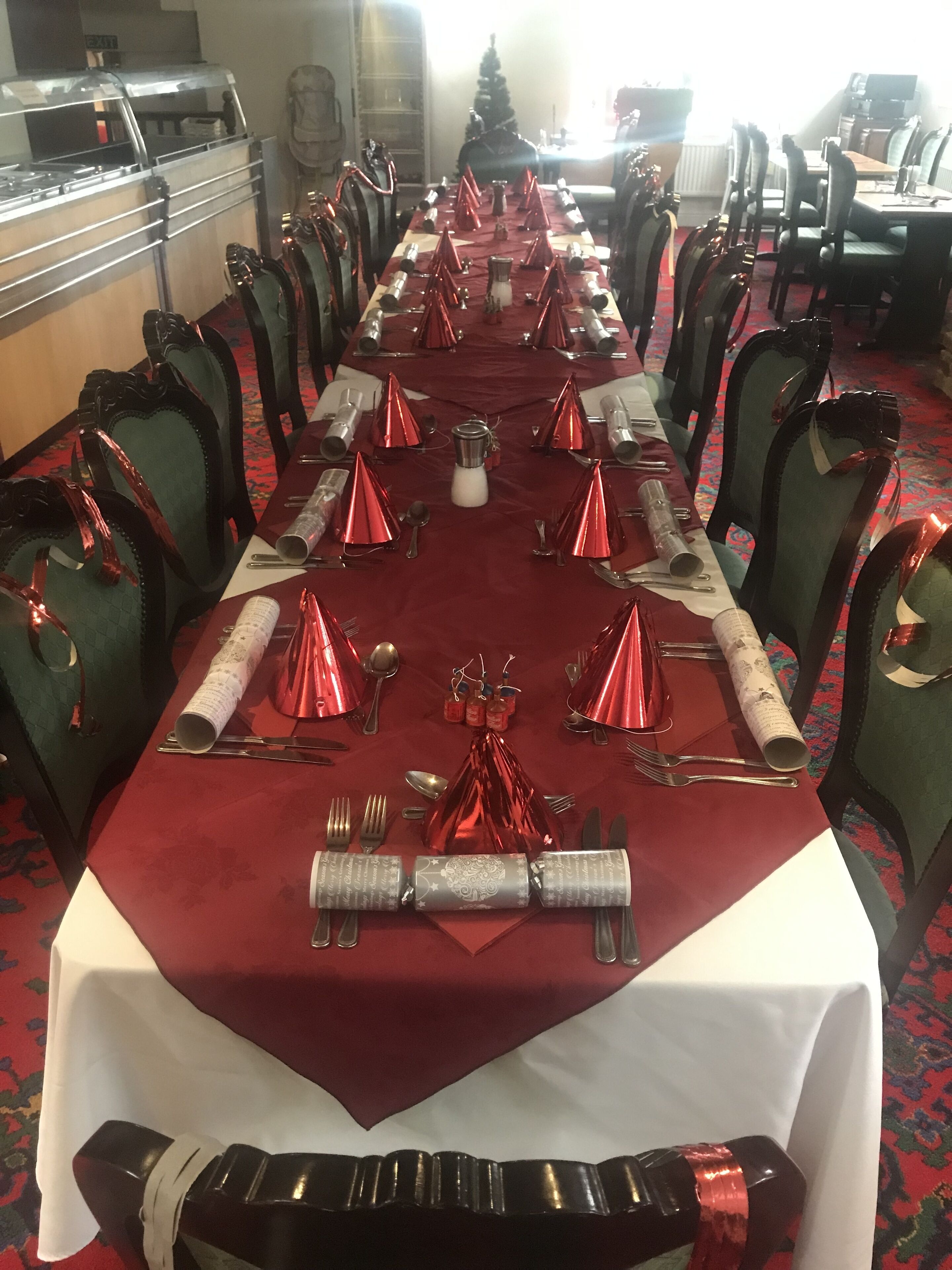 Una larga mesa de comedor dispuesta para un evento formal, rodeada de sillas tapizadas en verde.