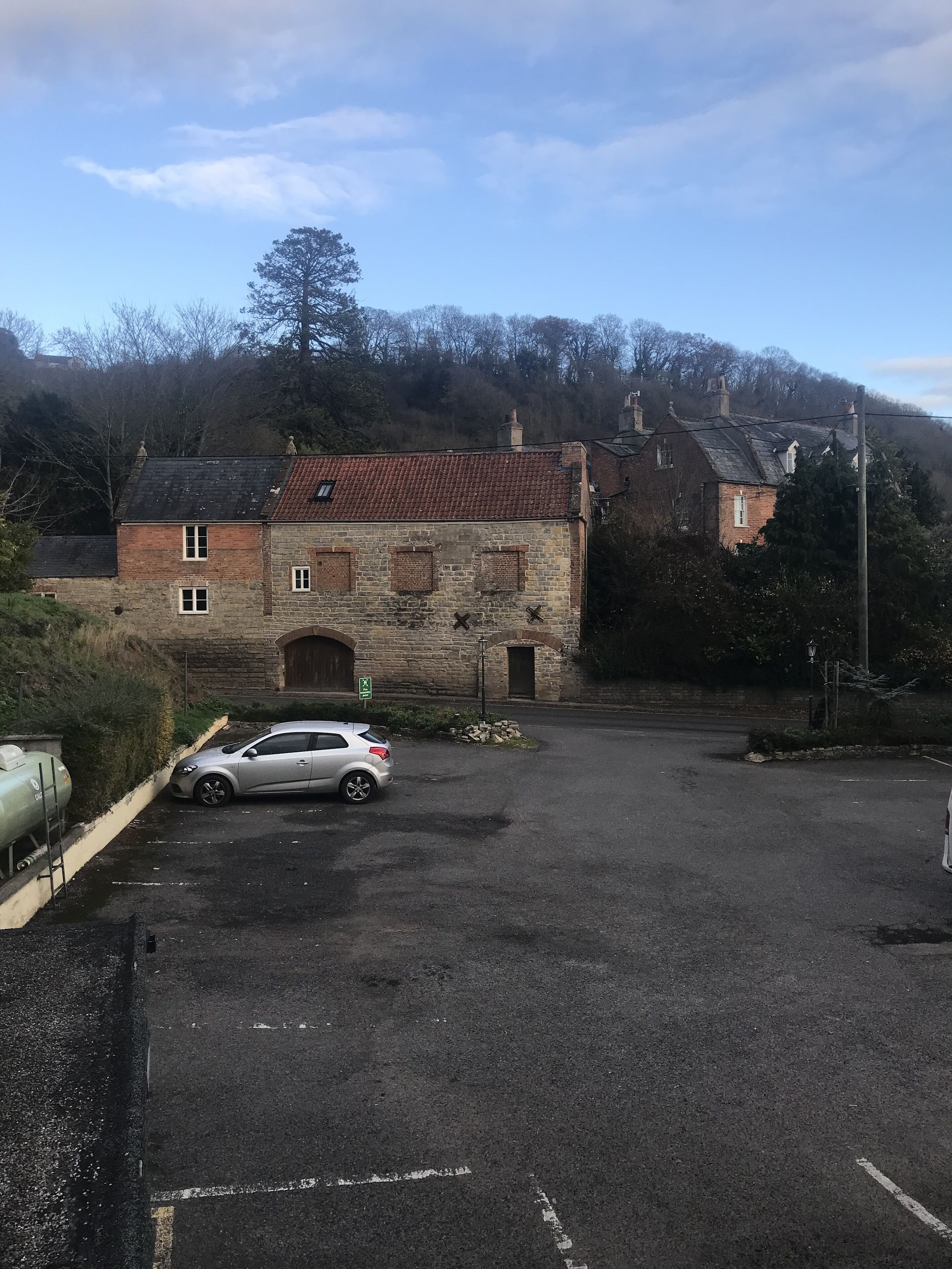 Un estacionamiento con un edificio de piedra, un automóvil y un letrero verde.