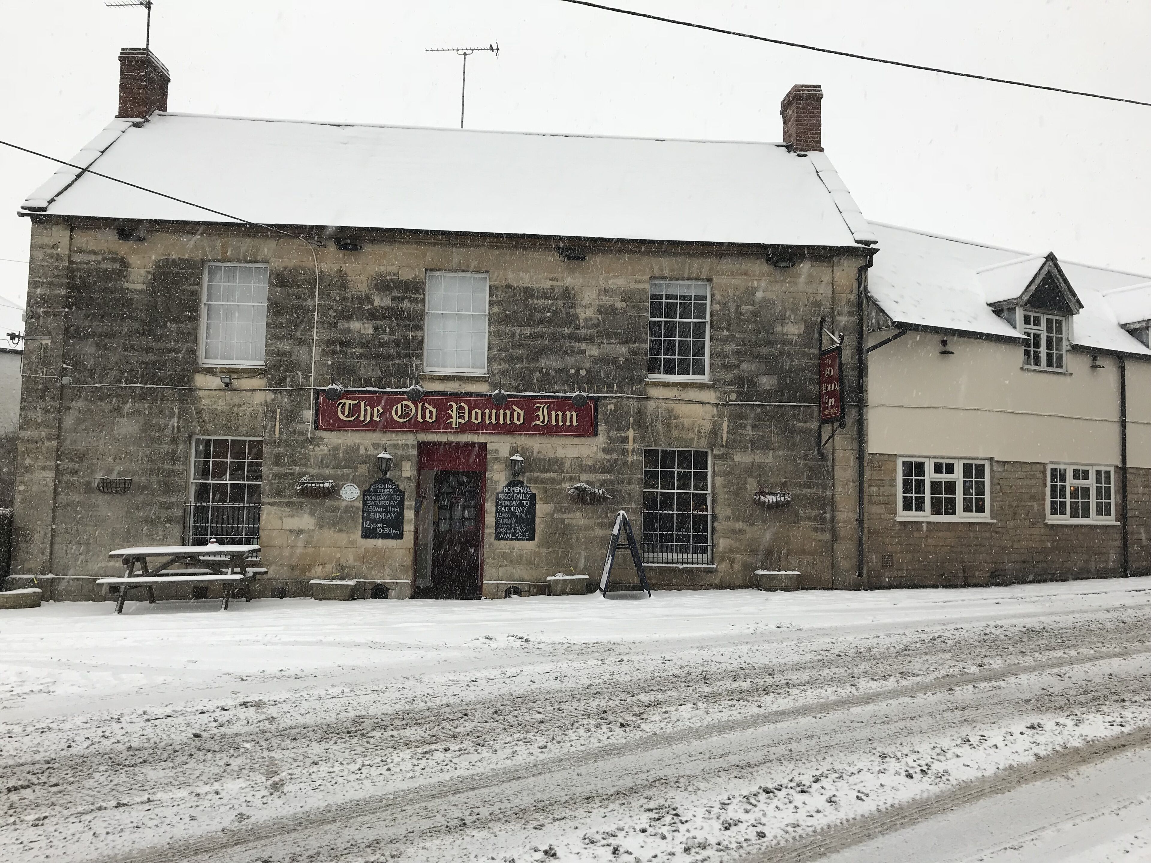 A stone building with a sign reading "The Old Pound Inn." There are benches outside and a ladder leaning against the building.