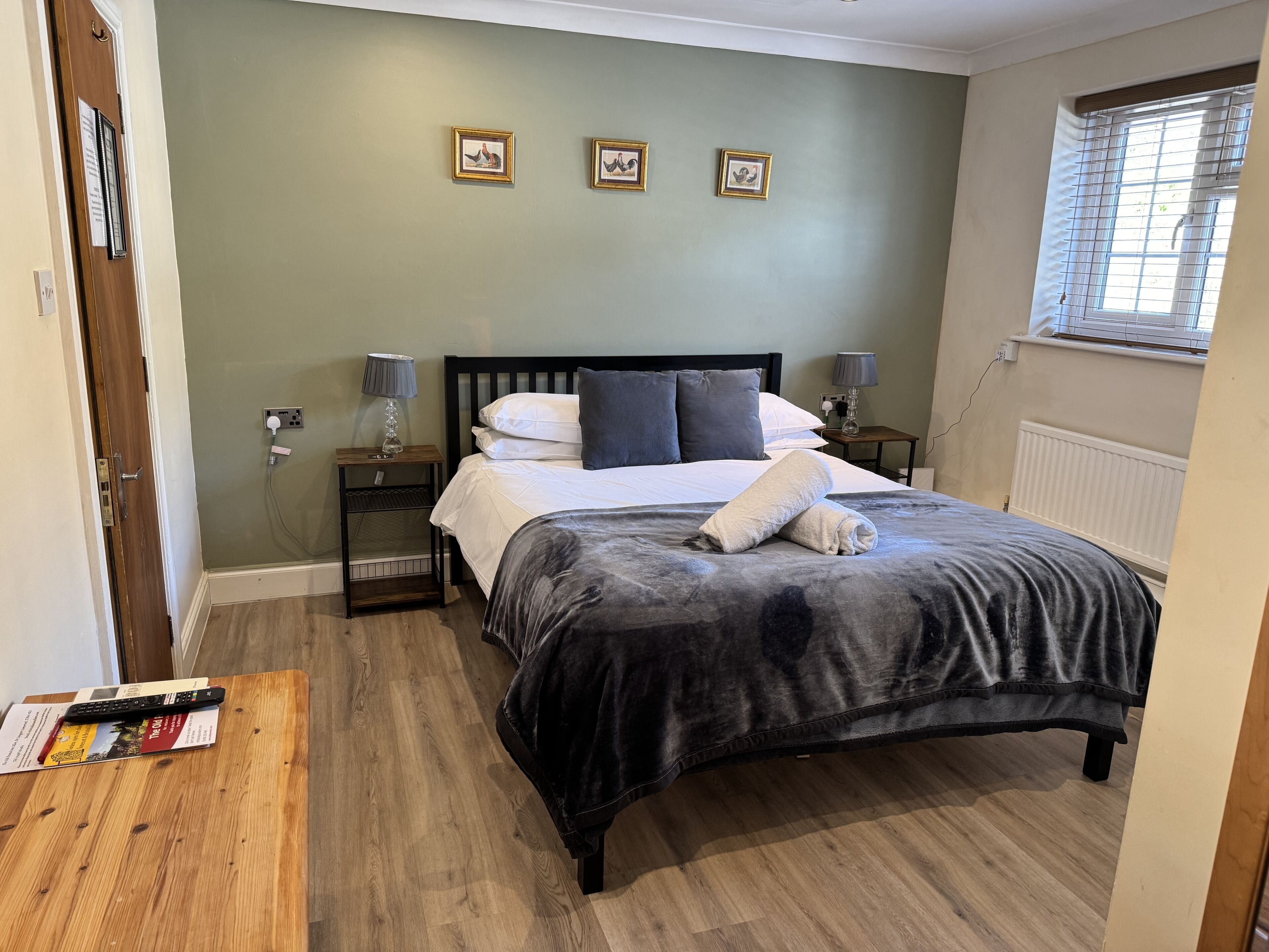 Un dormitorio con cama, lámparas de noche, una mesita de noche de madera, una ventana con persianas y tres cuadros en la pared.