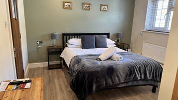 Un dormitorio con cama, lámparas de noche, una mesita de noche de madera, una ventana con persianas y tres cuadros en la pared.