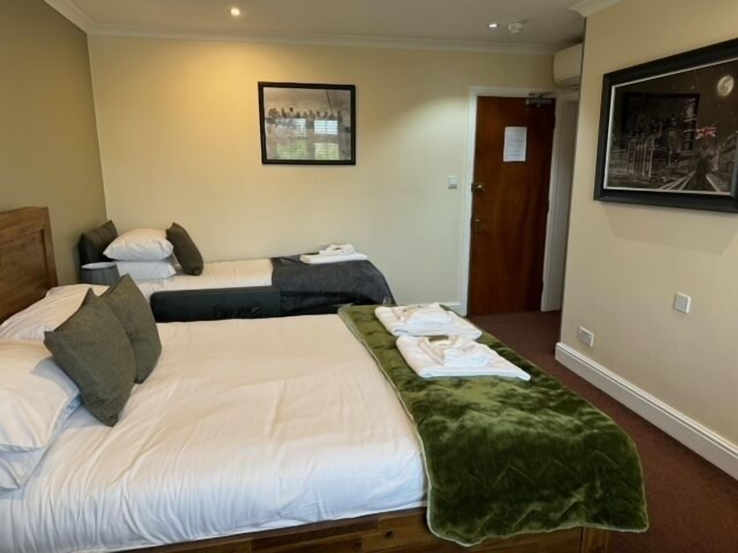 A hotel room with two beds, a green throw blanket, and a framed picture on the wall.