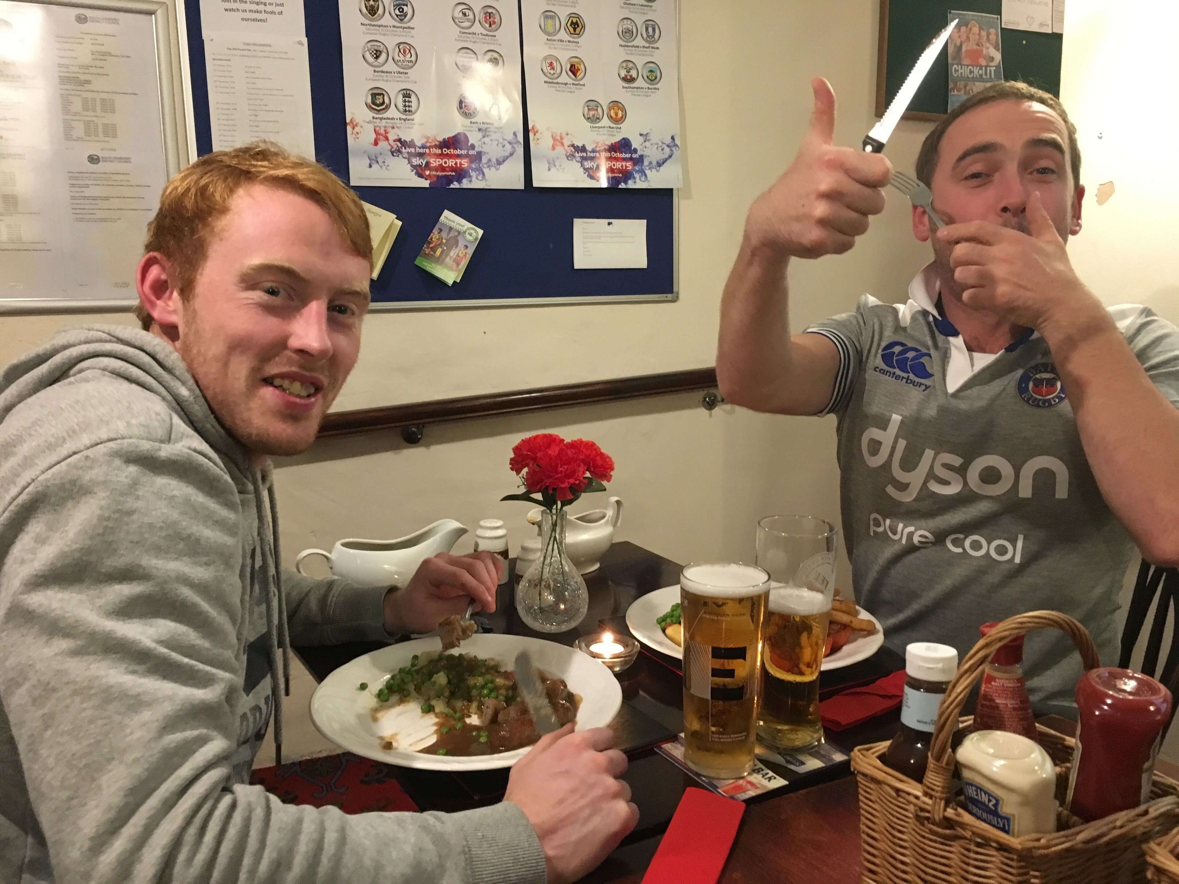 Two people at a table with food and drinks, a wall with sports memorabilia, and a candle on the table.