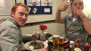 Two people at a table with food and drinks, a wall with sports memorabilia, and a candle on the table.