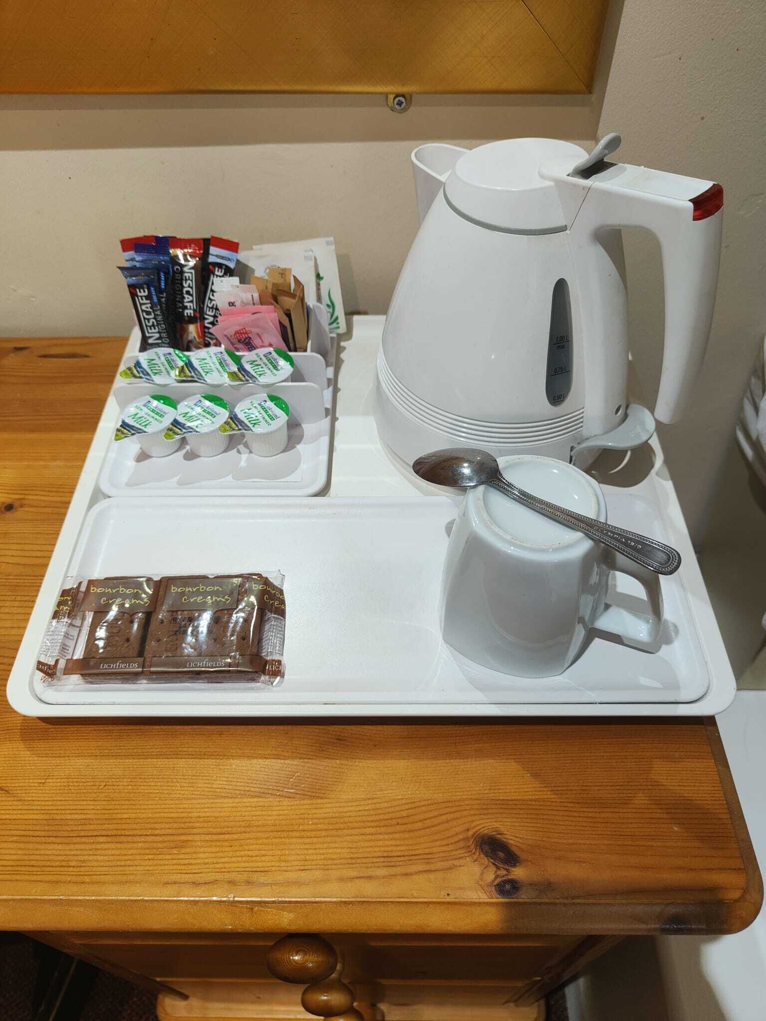 Una bandeja con cafetera, una taza, una cuchara y alimentos envasados sobre una mesa de madera.