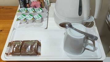 Una bandeja con cafetera, una taza, una cuchara y alimentos envasados sobre una mesa de madera.