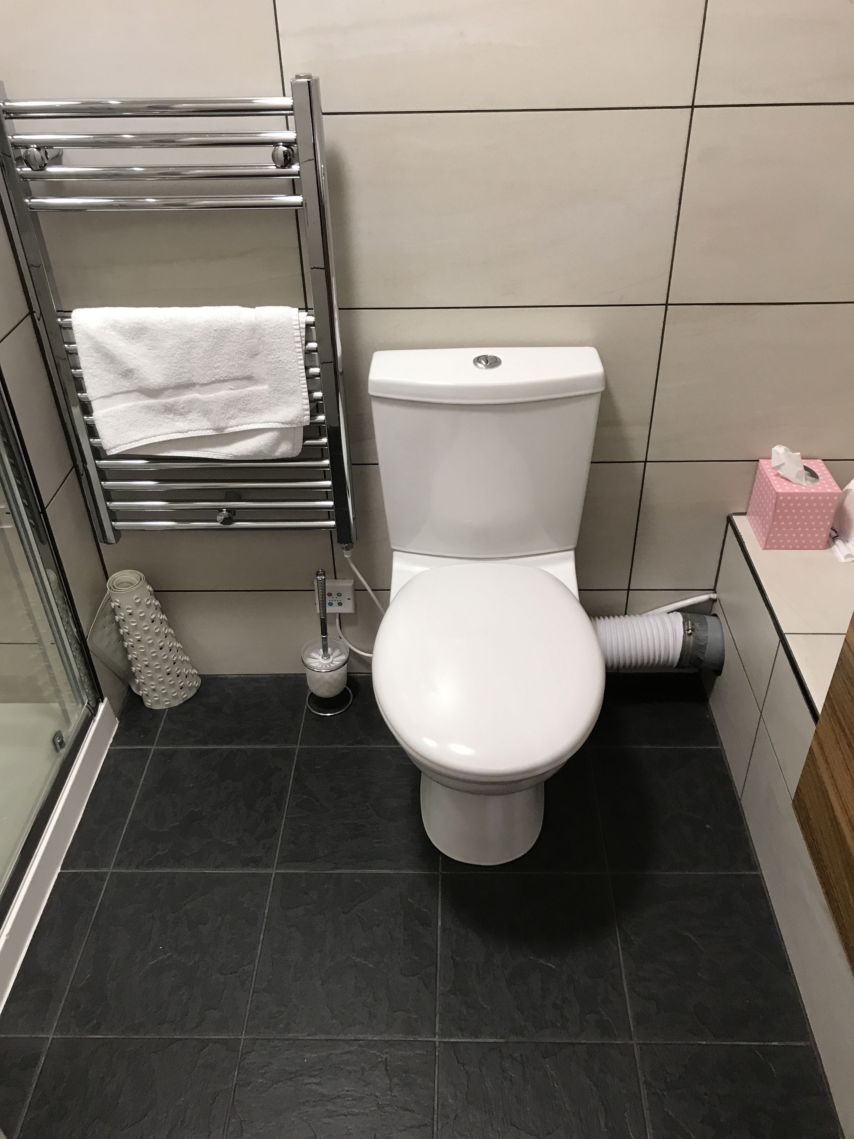 A modern bathroom with a white toilet, a towel rack, a toilet brush, and a hand dryer.
