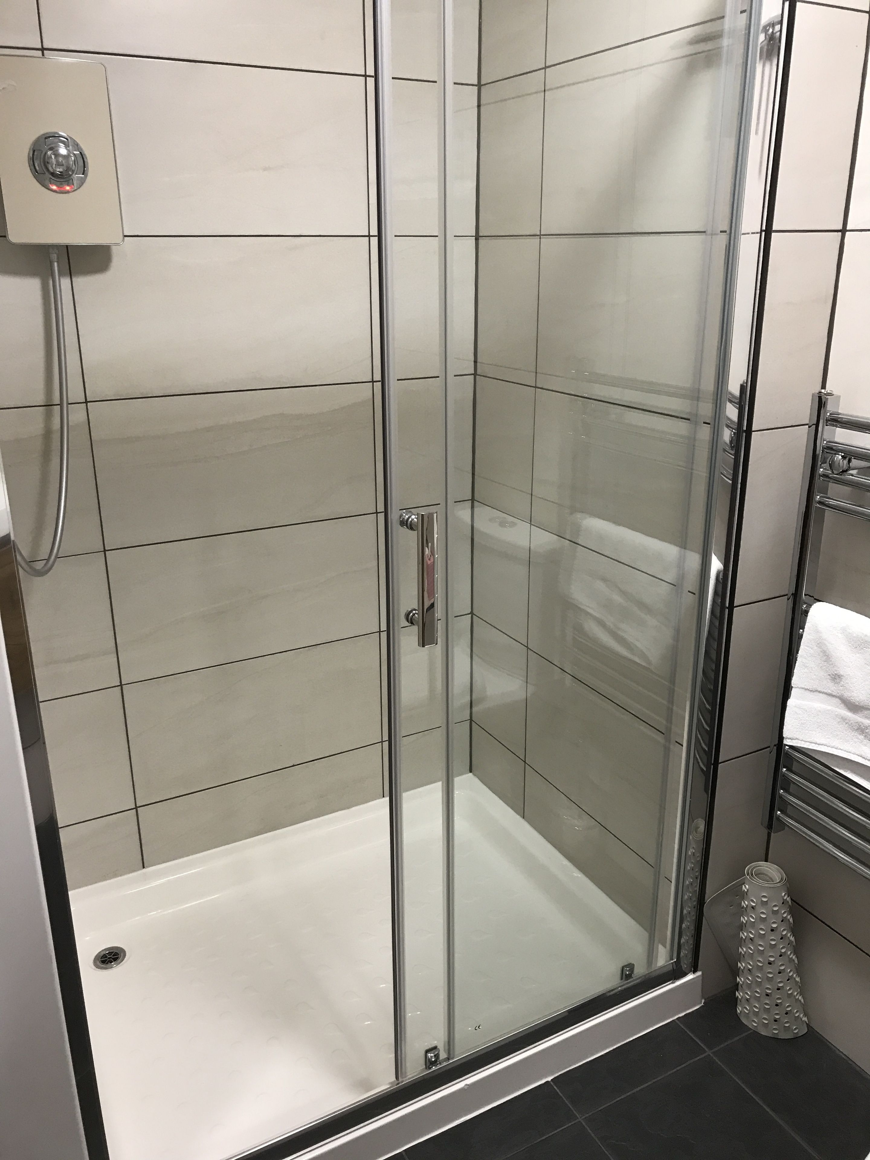 Une douche fermée par des parois de verre, dotée d’un panneau de commande, d’un sol carrelé et d’un porte-serviettes avec une serviette blanche.