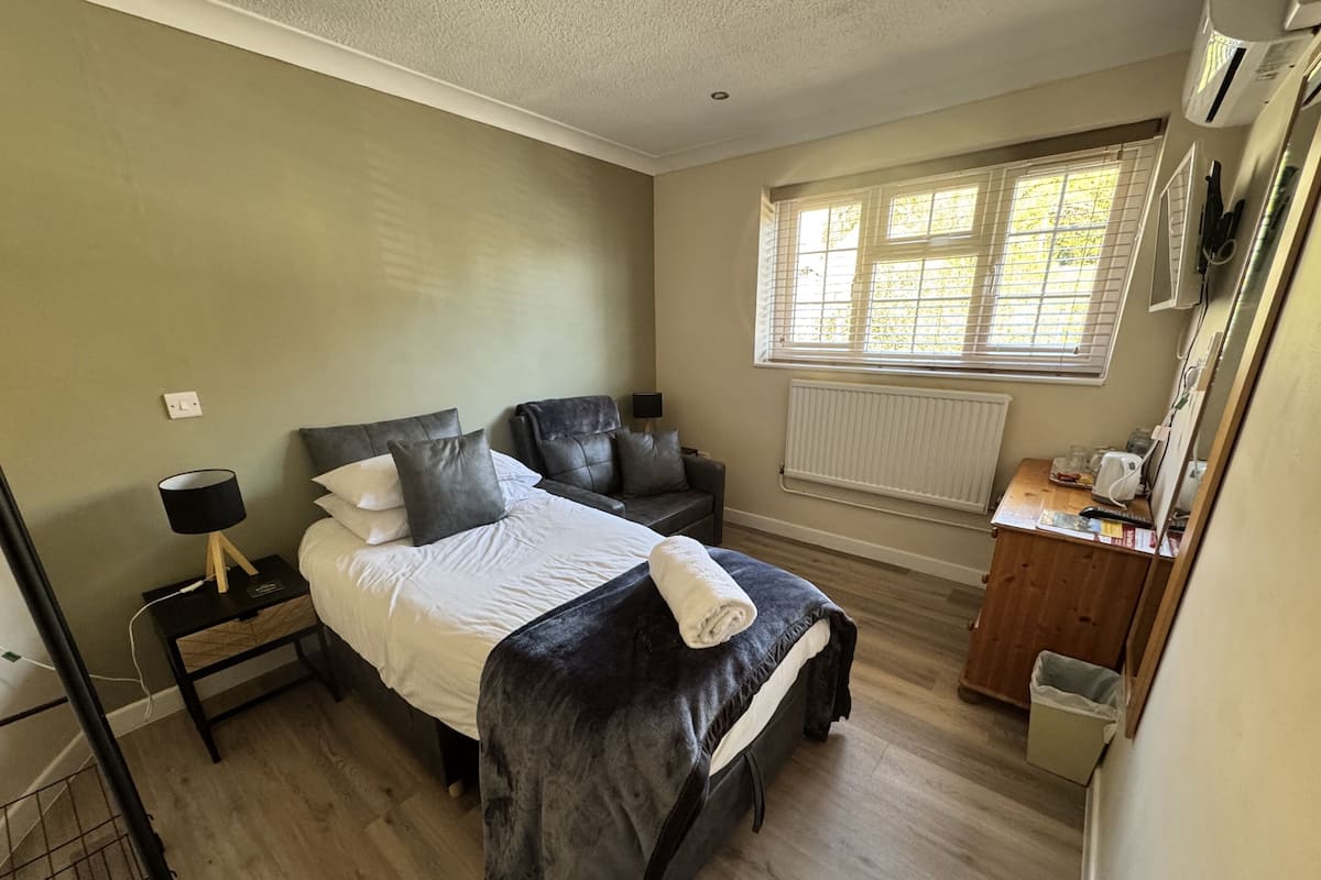 A bedroom with a bed, a chair, a desk, a radiator, and a window.
