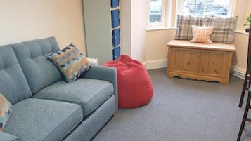 A living room with a blue sofa, red bean bag, and a wooden bench with cushions.
