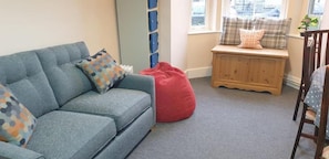 A living room with a blue sofa, red bean bag, and a wooden bench with cushions. - CellB - Hostel (Blaenau Ffestiniog)