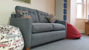 A grey sofa with patterned cushions, a red bean bag, and a map on the wall. - CellB - Hostel (Blaenau Ffestiniog)
