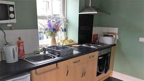 A compact kitchen with a sink, stove, and microwave. There is a window with a view of buildings outside. - CellB - Hostel (Blaenau Ffestiniog)