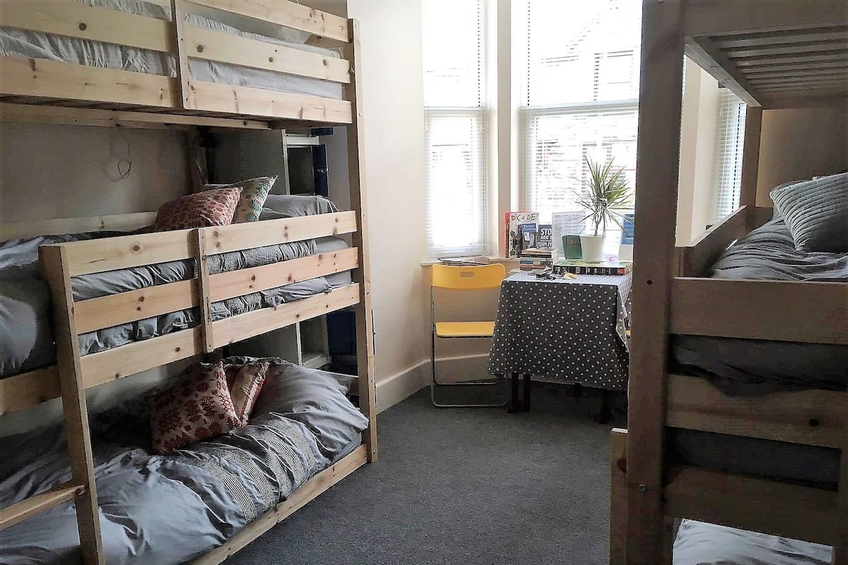 Um quarto de dormitório com beliches, uma escrivaninha pequena e uma cadeira.