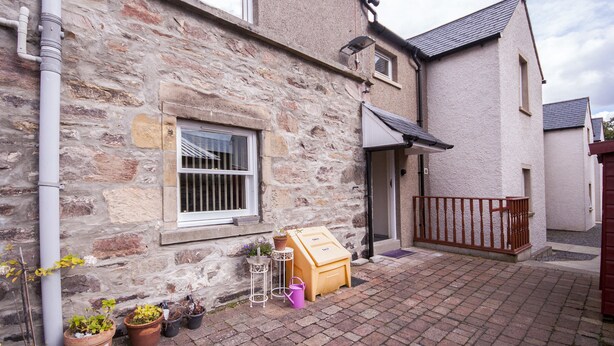 A stone building with a wooden bench and potted plants outside. - 3 Varis Apartments (Forres)