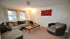 A living room with a sofa, armchair, and a coffee table. - 3 Varis Apartments (Forres)
