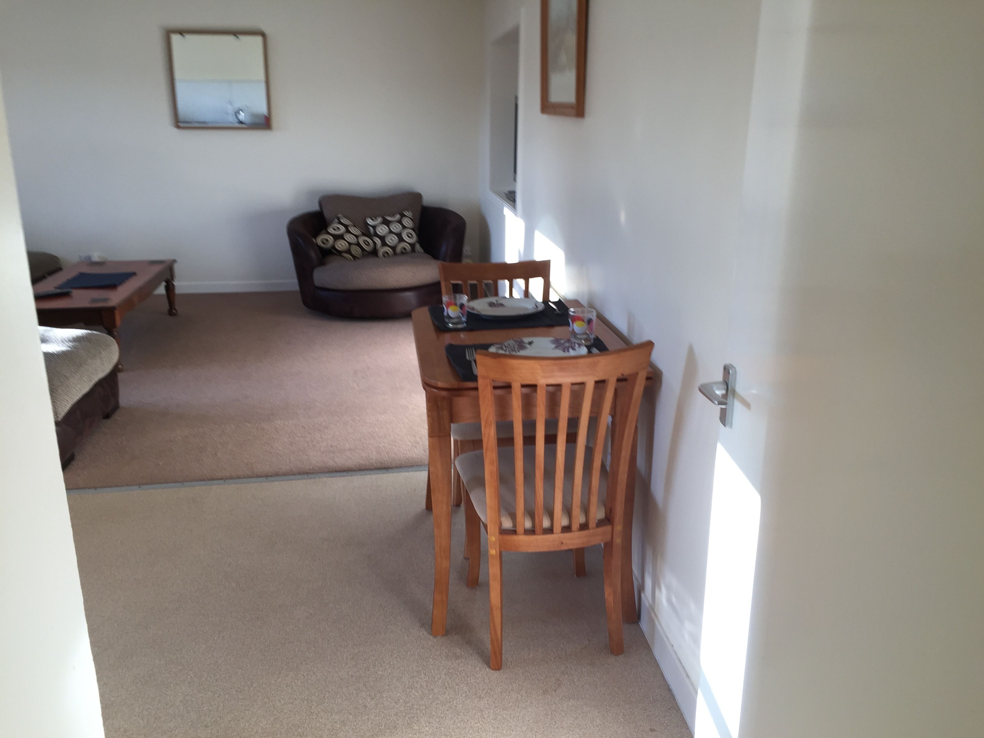 A dining area with a wooden table and chairs, a sofa with patterned cushions, and a mirror on the wall.