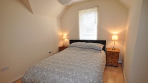 A bedroom with a bed, two bedside tables with lamps, a window with blinds, and a wooden floor. - 3 Varis Apartments (Forres)