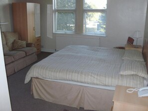 A bedroom with a bed, a wardrobe, a chair, a window, and a bedside table. - Heritage Hotel (Leicester)