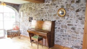 A room with a stone wall, a wooden piano, a chair, and a large window. - Glynhir Mansion (Ammanford)