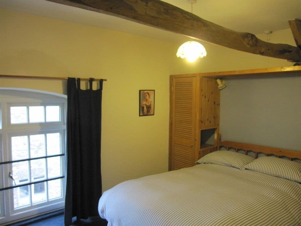 A bedroom with a bed, a window with curtains, a wooden headboard, and a ceiling light.