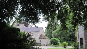 A rural house with a gravel driveway, surrounded by lush greenery and trees. - Glynhir Mansion (Ammanford)