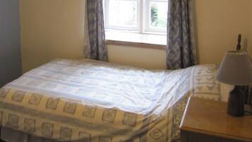 A small bedroom with a bed, a nightstand, a lamp, and a window with curtains.