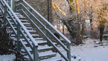 Un bâtiment en pierre avec un escalier menant à une porte, entouré d’un sol couvert de neige et d’arbres sans feuilles.
