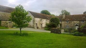 A stone building with a sloped roof, a paved driveway, and a grassy area in front.